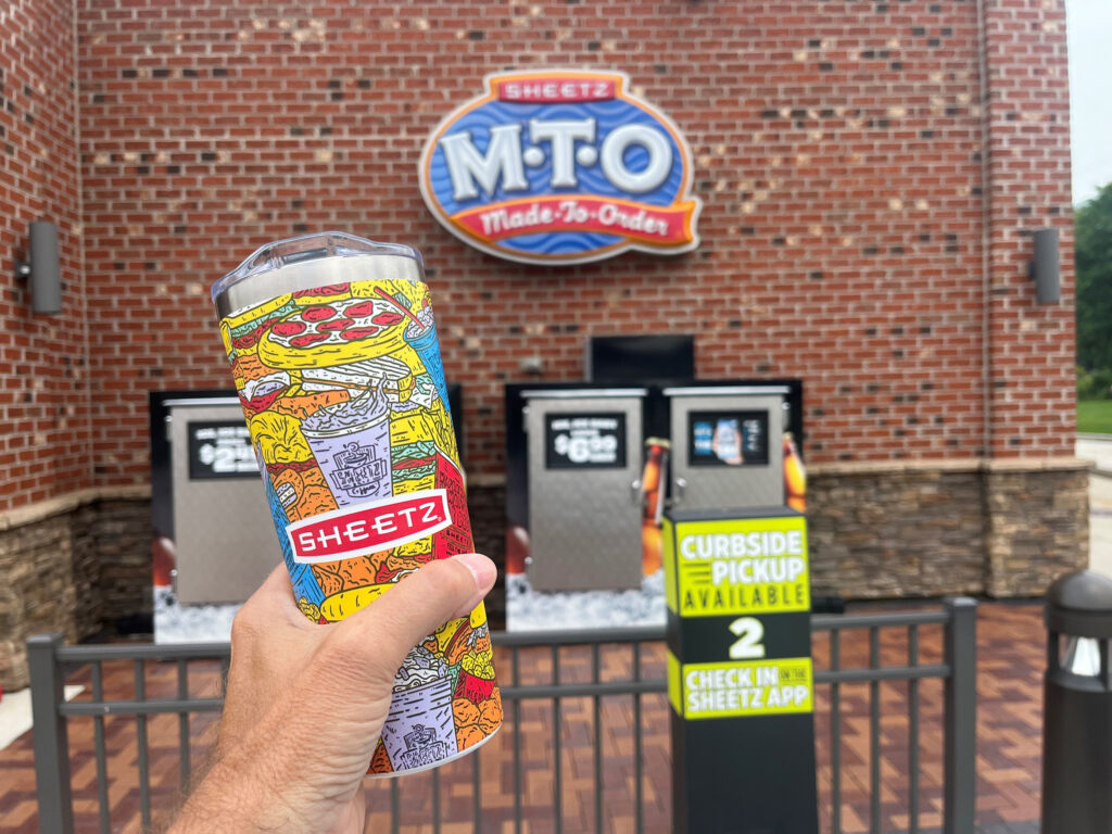 Person holding a Whirley-DrinkWorks! cup outside a convenience store.